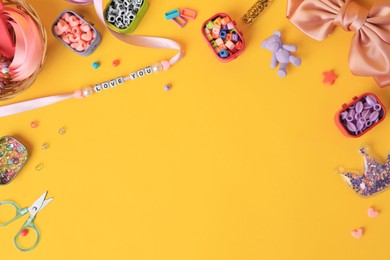 Kid`s handmade jewelry kit. Colorful beads, ribbon, bow and different supplies on orange background, flat lay. Space for text