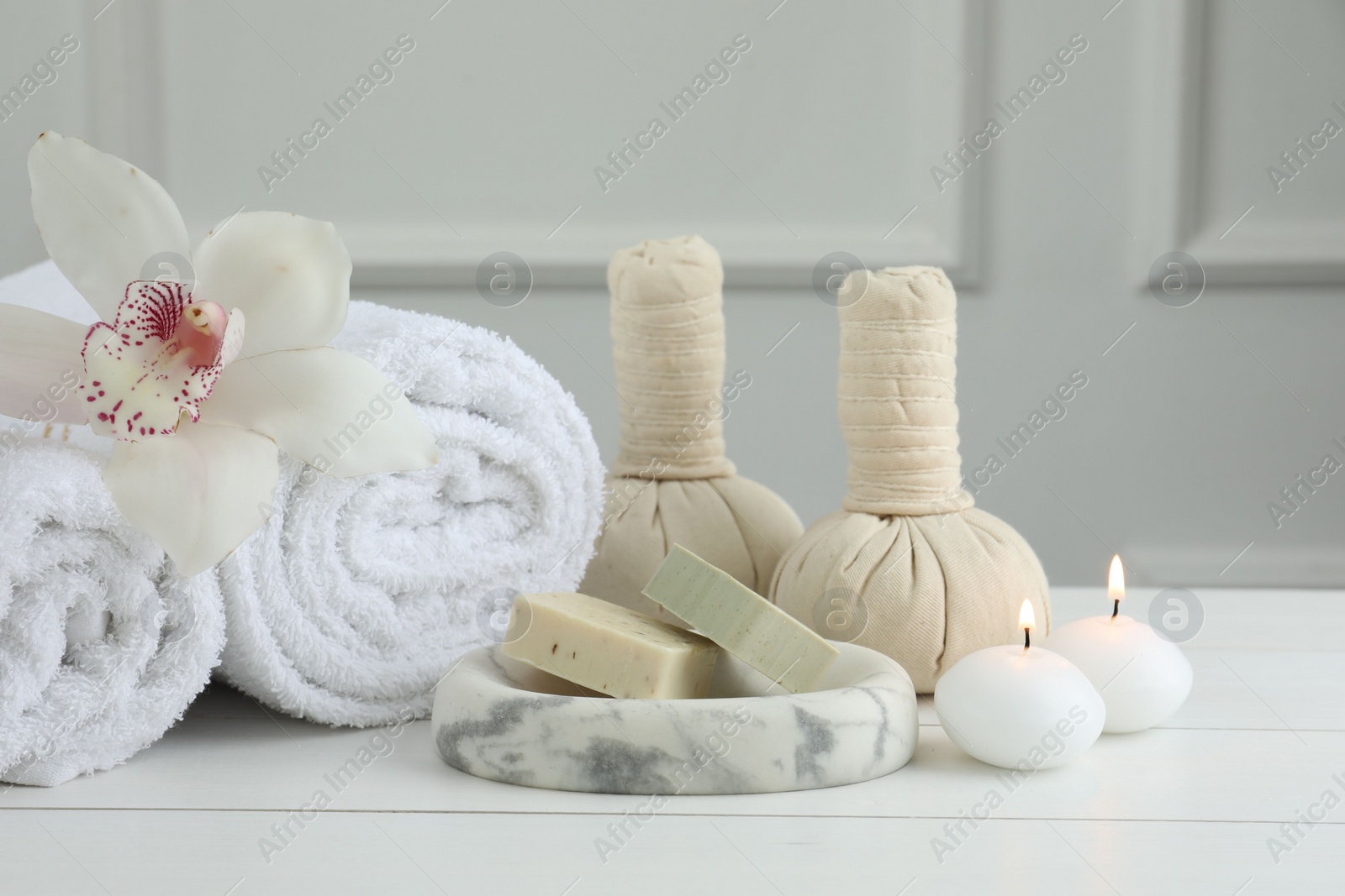 Photo of Beautiful spa composition. Towels, herbal bags, soap bars and burning candles on white wooden table