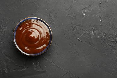 Photo of Tasty barbeque sauce in bowl on dark textured table, top view. Space for text