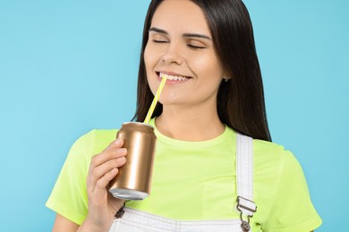 Beautiful happy woman drinking from beverage can on light blue background