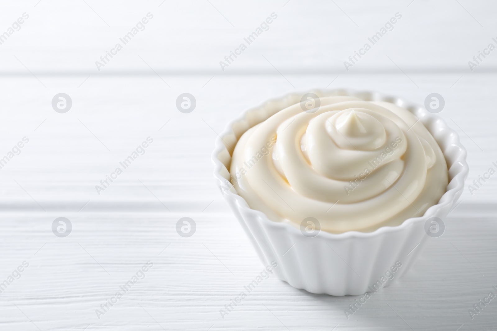 Photo of Fresh mayonnaise sauce in bowl on white wooden table, closeup. Space for text