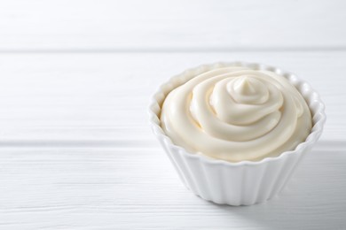 Photo of Fresh mayonnaise sauce in bowl on white wooden table, closeup. Space for text