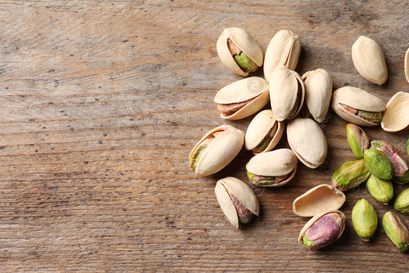 Photo of Organic pistachio nuts on wooden table. Space for text