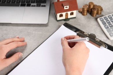 Photo of Woman planning budget, closeup. House model and coins on grey table