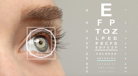 Vision test chart and laser reticle focused on woman's eye against light grey background, closeup