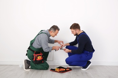 Senior electrician helping trainee stripping wire ends indoors