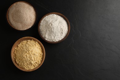 Photo of Different types of flours on black table, flat lay. Space for text