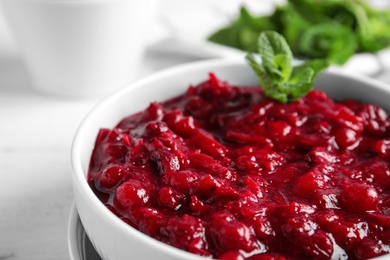 Photo of Bowl of tasty cranberry sauce with mint on table, closeup