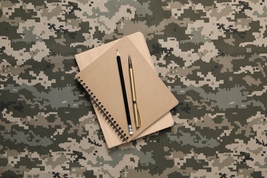 Notebooks, pen and pencil on camouflage background, top view. Military education