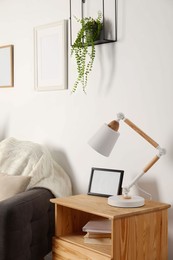 Photo of Stylish modern desk lamp and frame on wooden cabinet near armchair indoors