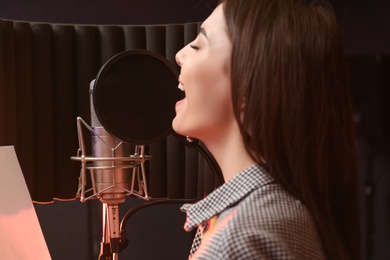 Photo of Young singer with microphone recording song in studio