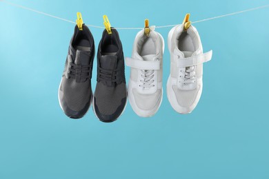 Different stylish sneakers drying on washing line against light blue background