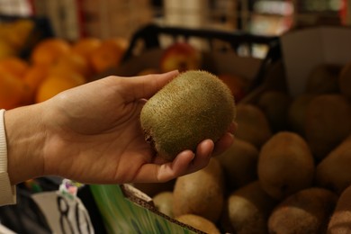 Woman holding fresh kiwi near fruit counter at market, closeup