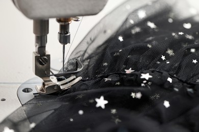 Photo of Sewing machine and black fabric with paillettes, closeup