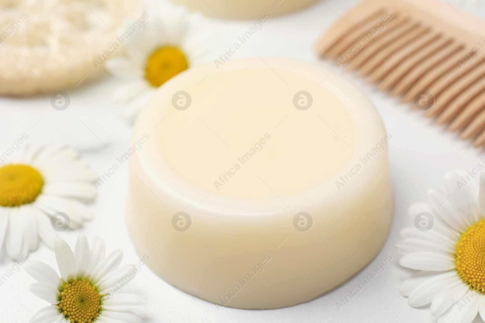 Photo of Solid shampoo bar, comb and chamomiles on white table, closeup. Hair care