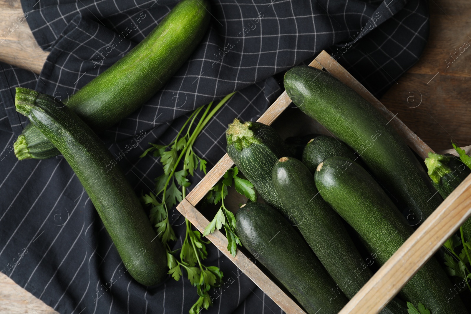 Photo of Crate with green zucchinis and parsley on table, flat lay