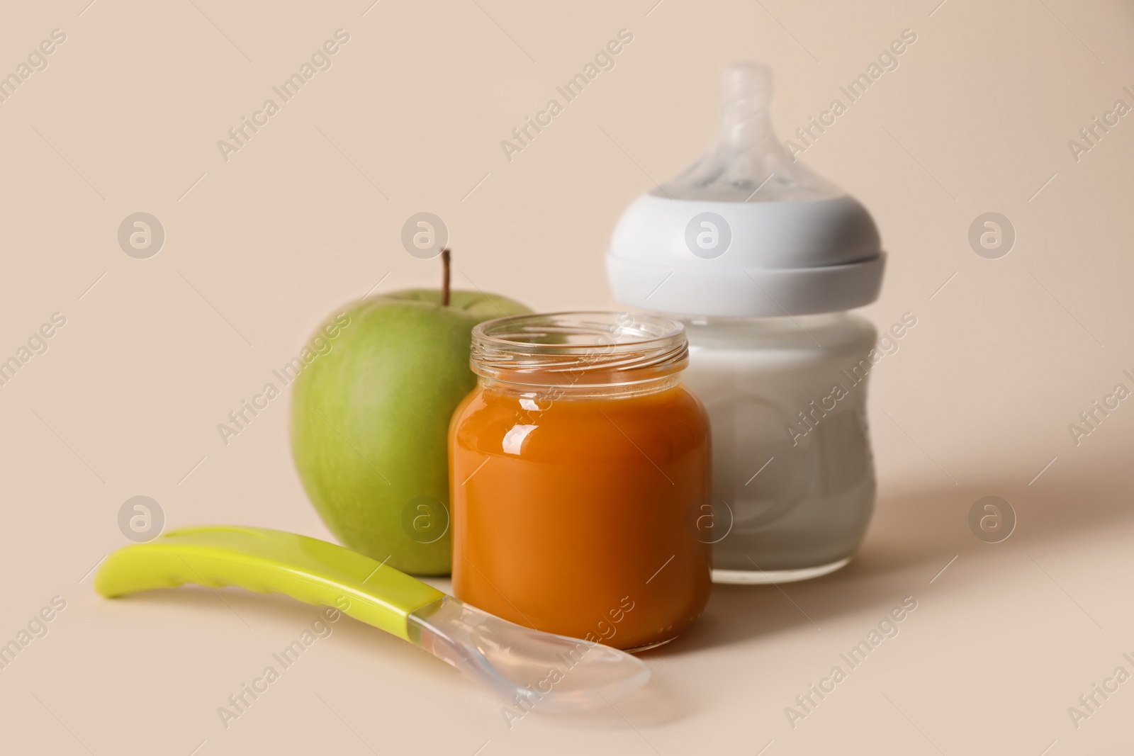 Photo of Healthy baby food in jar, bottle of milk, apple and spoon on beige background