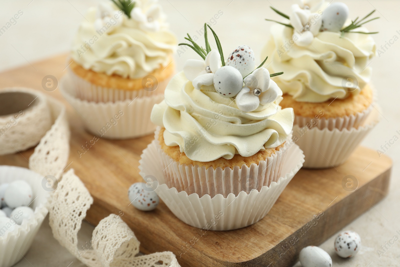 Photo of Tasty Easter cupcakes with vanilla cream, candies and ribbon on gray table, closeup