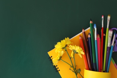 Different school stationery and beautiful yellow flowers on green chalkboard, flat lay with space for text. Happy Teacher's Day