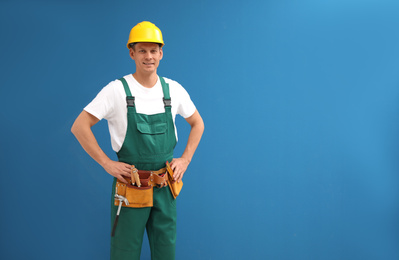 Handsome carpenter with tool belt on blue background. Space for text