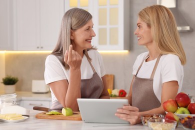 Photo of Happy mature mother and her daughter with tablet in kitchen