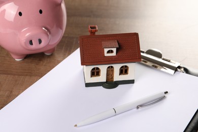 House model, piggy bank, clipboard and pen on wooden table