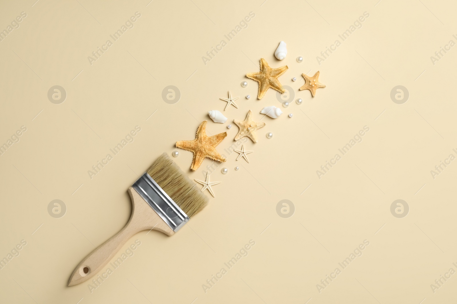 Photo of Brush painting with sea stars, pearls and shells on beige background, flat lay. Creative concept