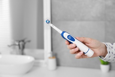 Photo of Woman holding electric toothbrush in bathroom at home, closeup