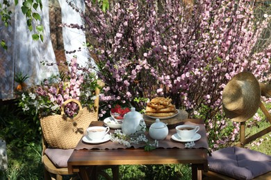 Photo of Beautiful spring flowers, freshly baked waffles and ripe strawberries on table served for tea drinking in garden