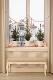 Photo of Small potted fir trees and Christmas decor on window sill indoors