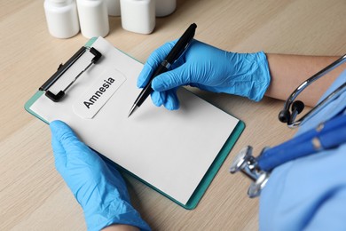 Photo of Doctor holding clipboard with word Amnesia at wooden table, closeup
