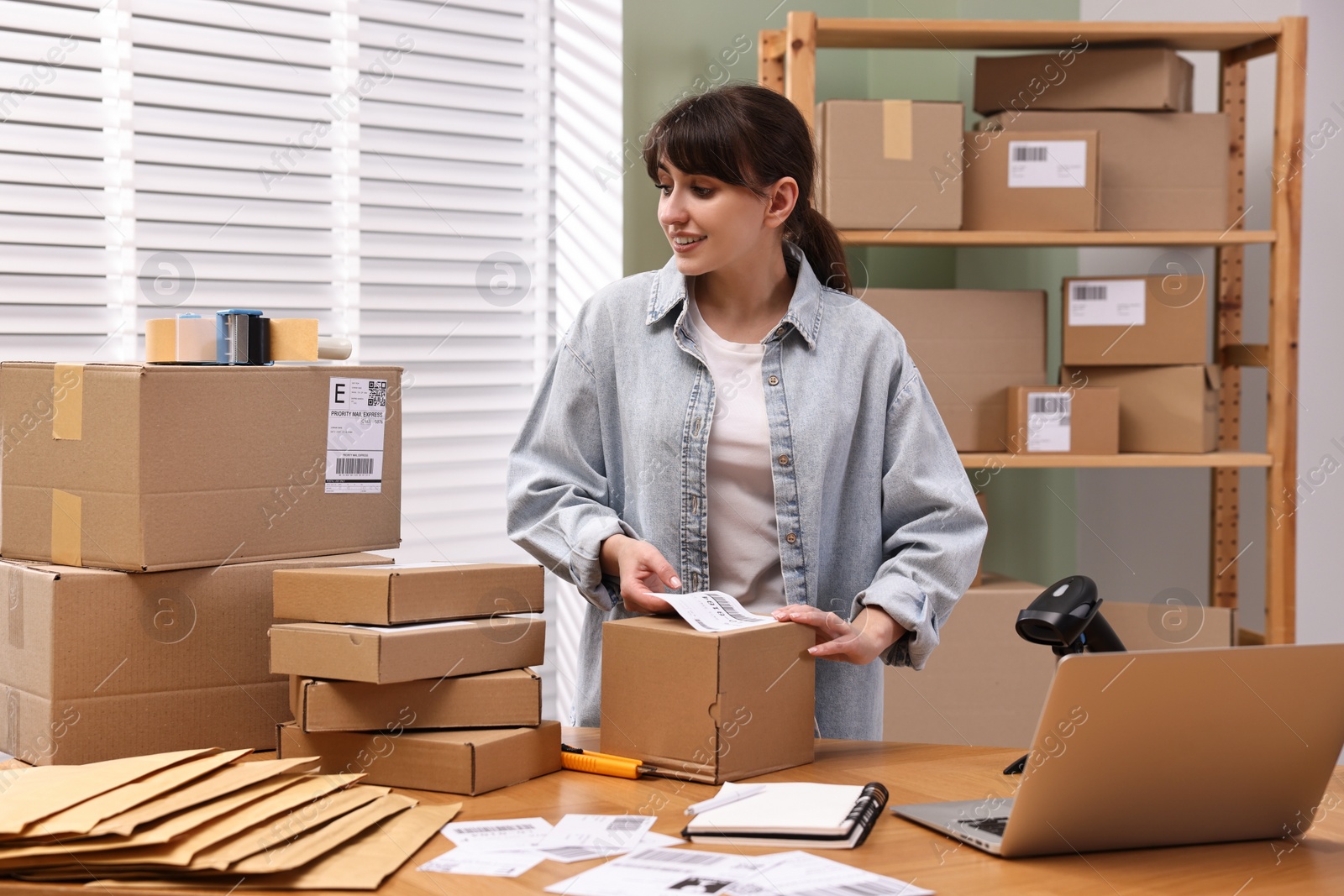 Photo of Parcel packing. Post office worker sticking barcode on box at wooden table indoors