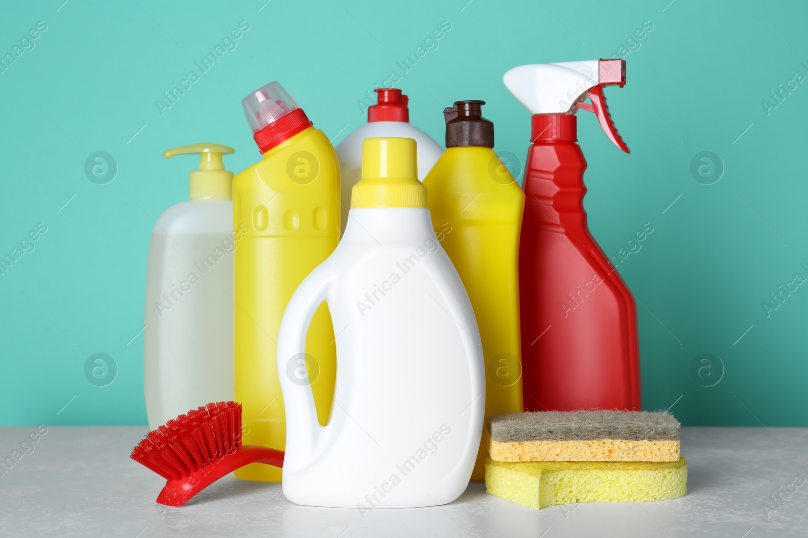 Photo of Different cleaning supplies and tools on table against turquoise background