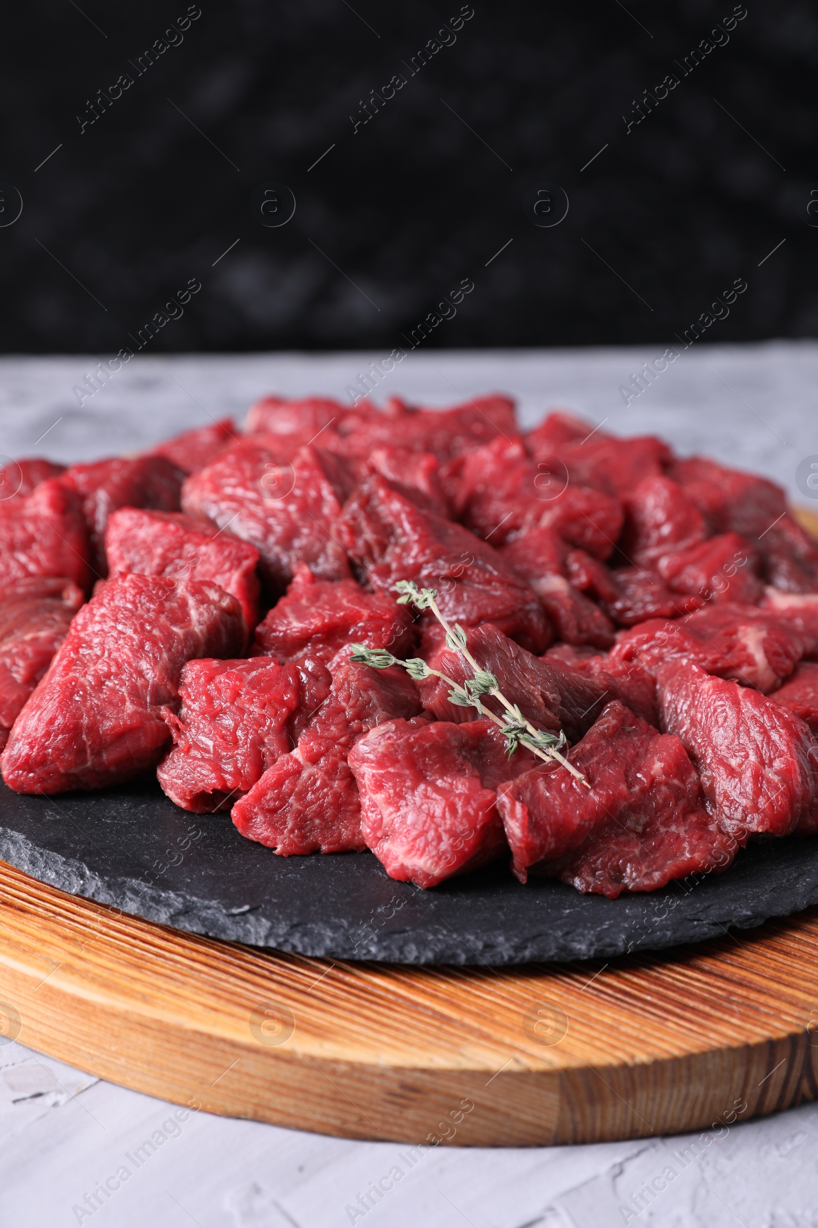 Photo of Pieces of raw beef meat and thyme sprigs on grey textured table against black background, closeup