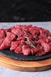 Pieces of raw beef meat and thyme sprigs on grey textured table against black background, closeup