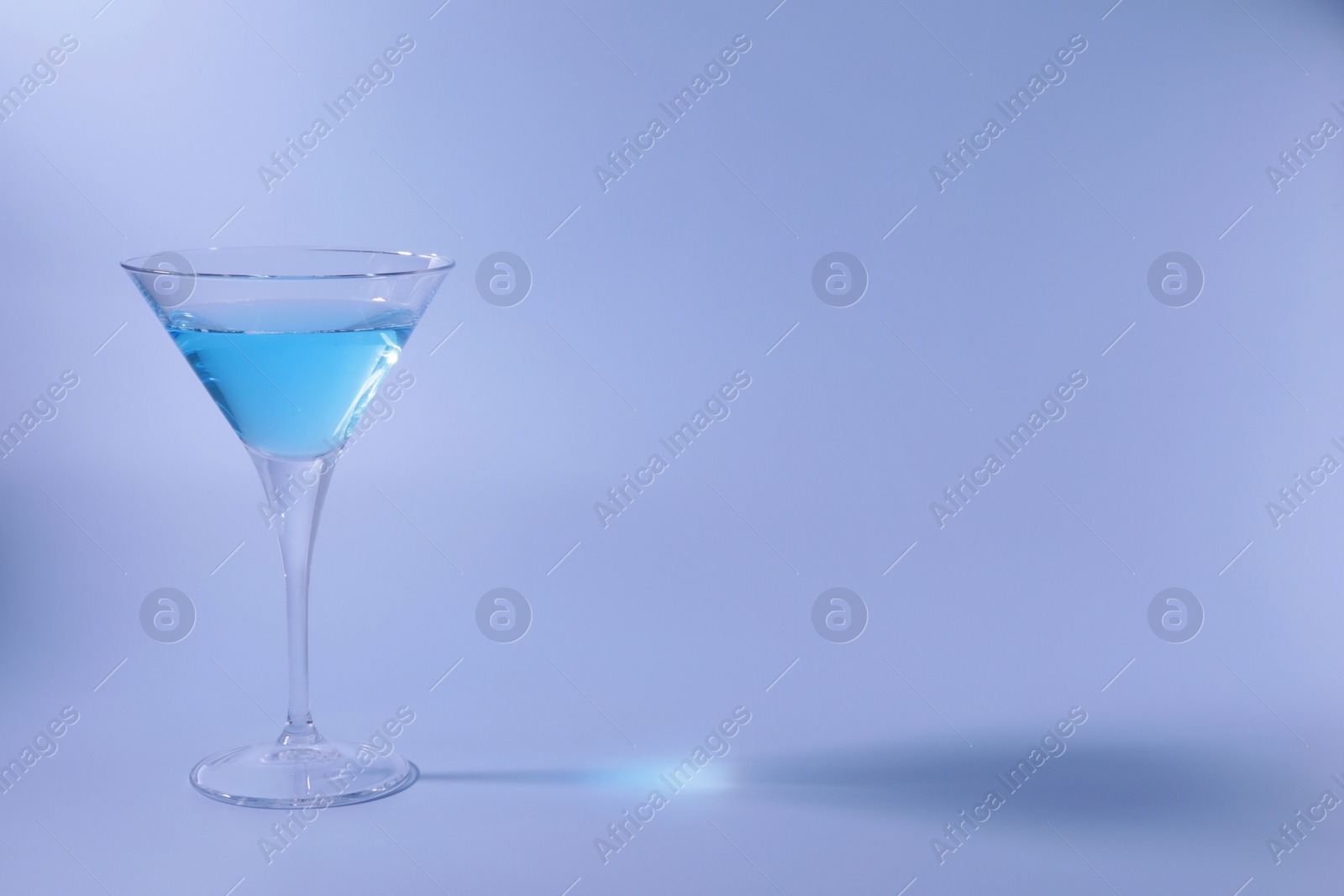 Photo of Martini glass with delicious cocktail on light blue background, space for text