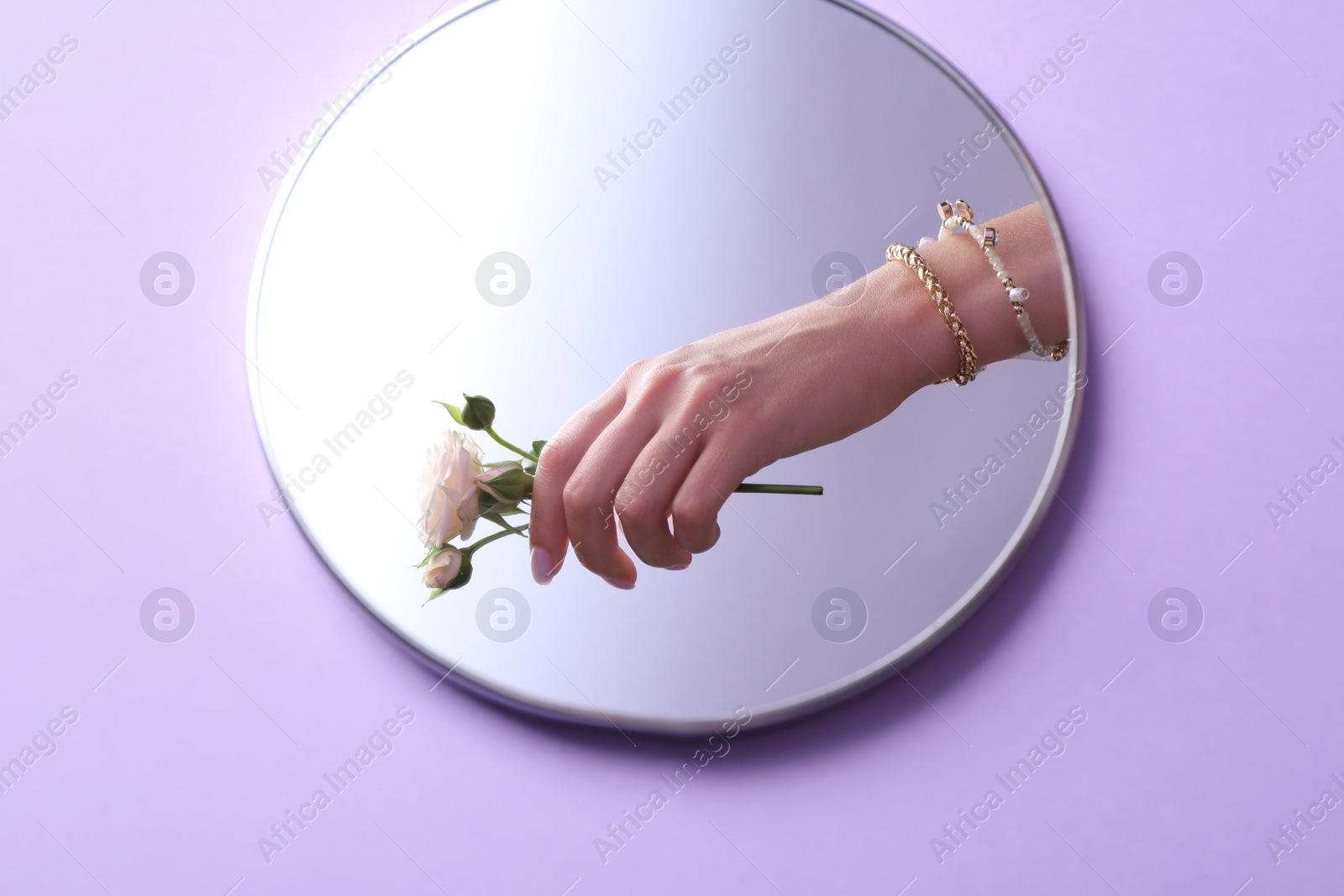 Photo of Reflection of woman with beautiful jewelry and flower in mirror on violet background, above view