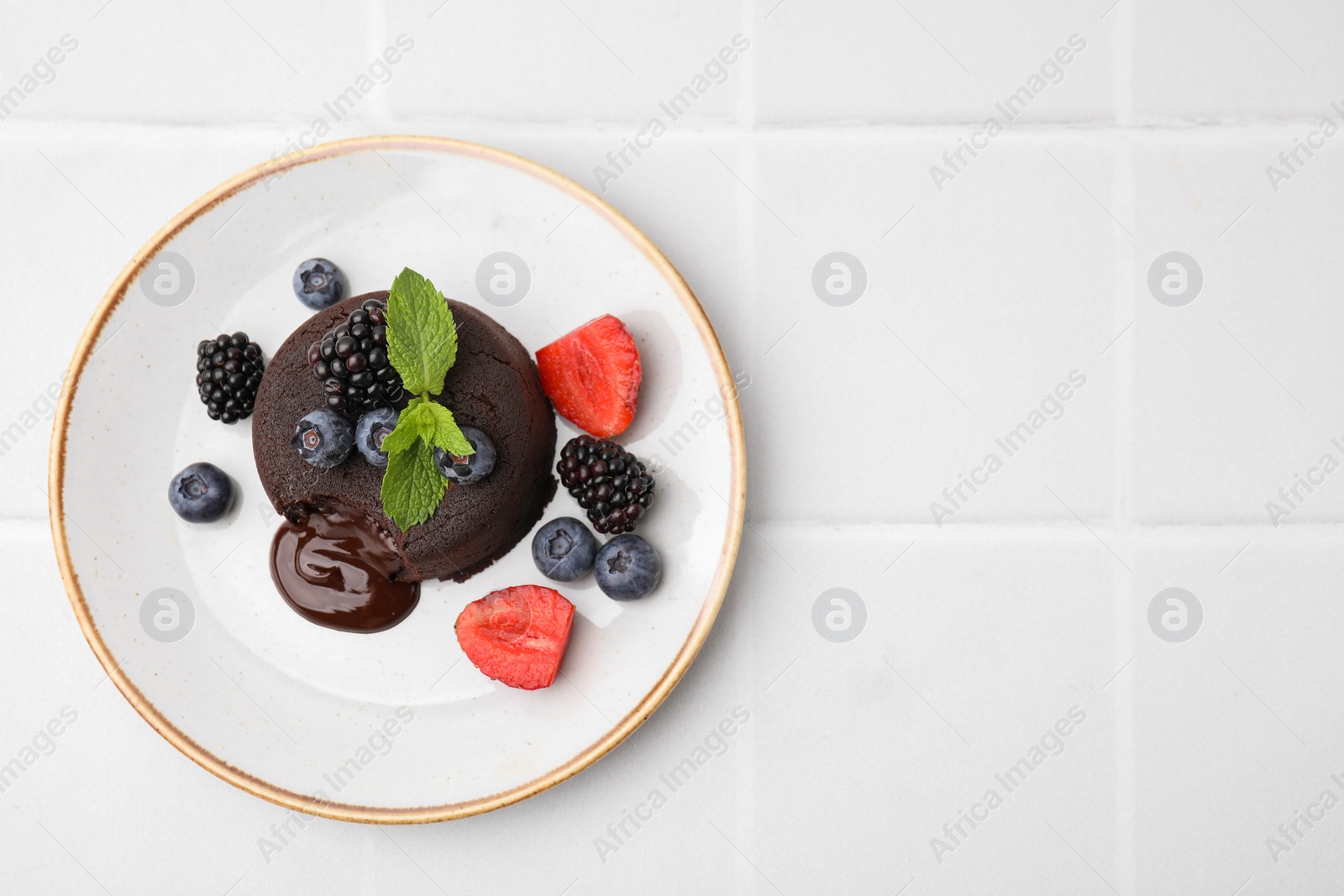 Photo of Plate with delicious chocolate fondant, berries and mint on white tiled table, top view. Space for text