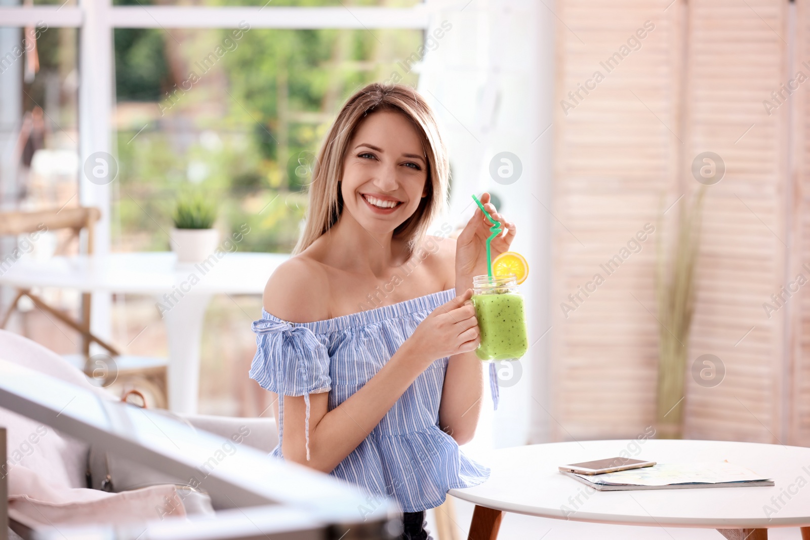 Photo of Young woman with tasty healthy smoothie at table, indoors