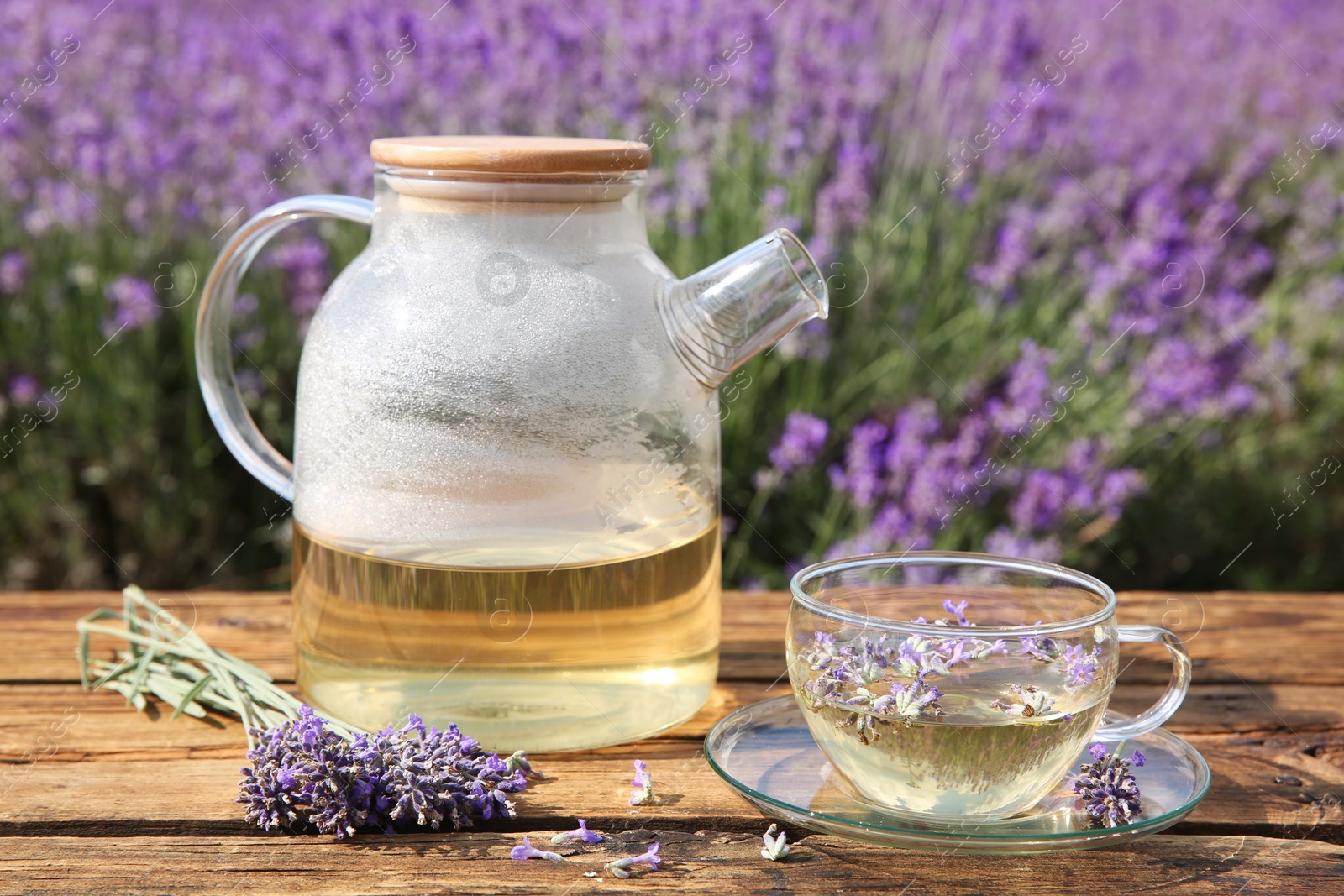 Photo of Tasty herbal tea and fresh lavender flowers on wooden table in field