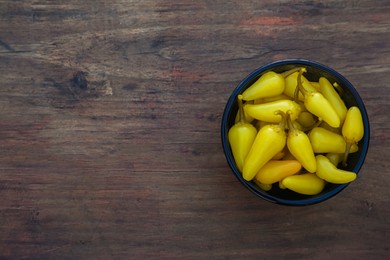 Photo of Bowl of pickled yellow jalapeno peppers on wooden table, top view. Space for text