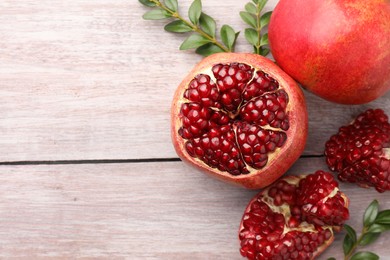 Photo of Fresh pomegranates and green leaves on wooden table, flat lay. Space for text
