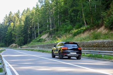 Picturesque view of asphalt road with modern black car near forest