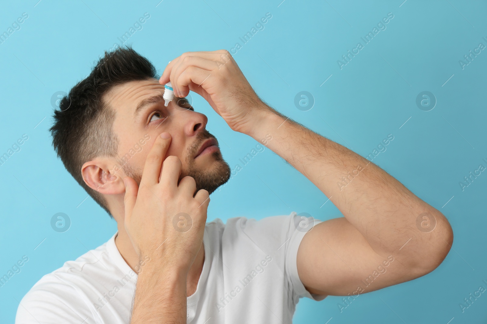 Photo of Man using eye drops on light blue background