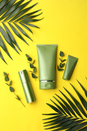 Photo of Set of cosmetic products and green leaves on yellow background, flat lay