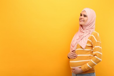 Portrait of pregnant Muslim woman in hijab on orange background, space for text