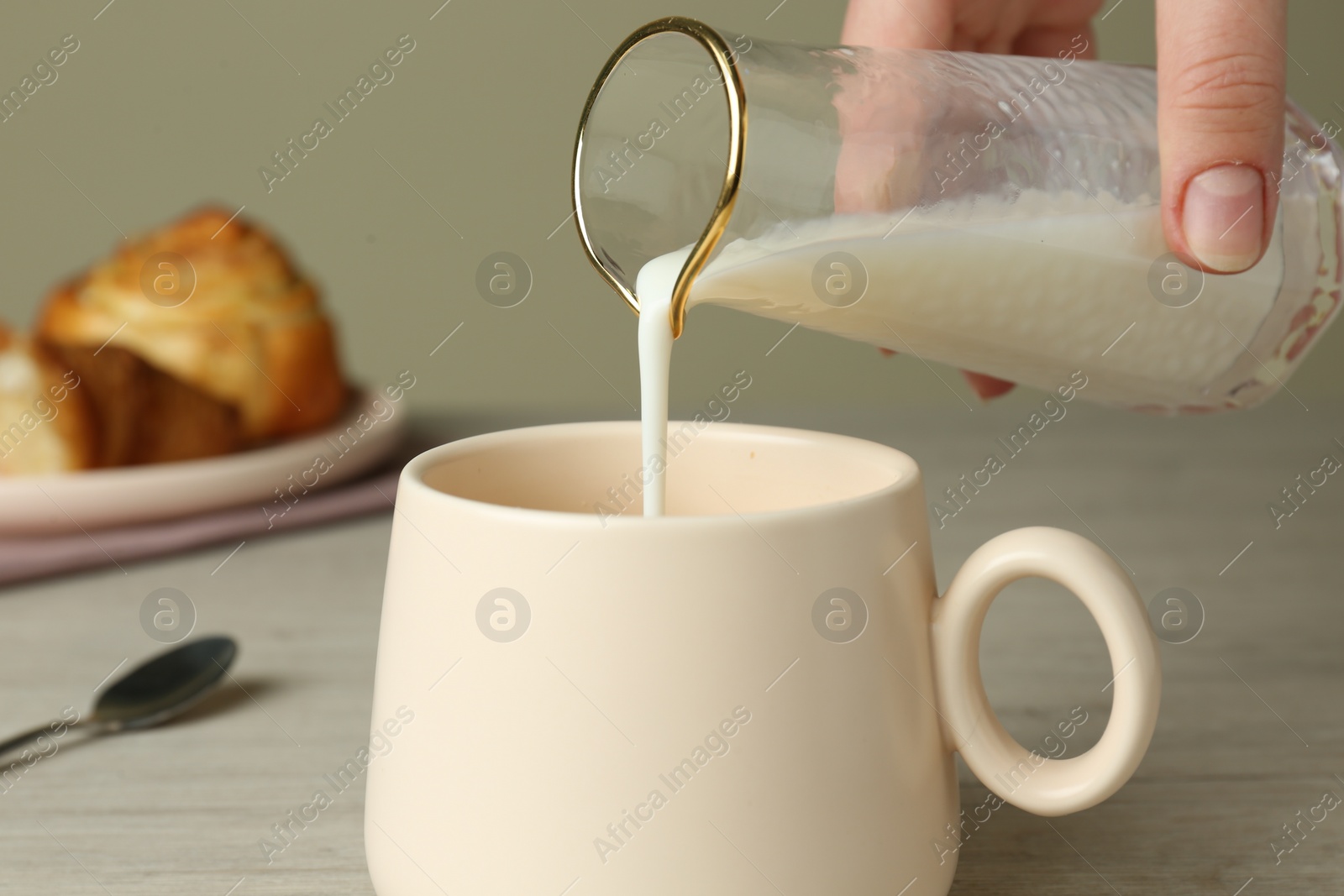 Photo of Woman pouring milk into cup at table, closeup