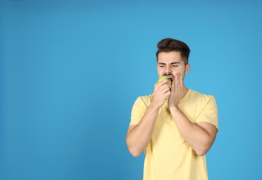 Emotional young man with sensitive teeth eating apple on color background. Space for text