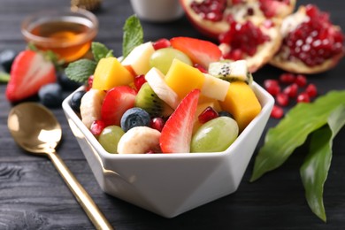 Photo of Delicious fresh fruit salad in bowl on black wooden table