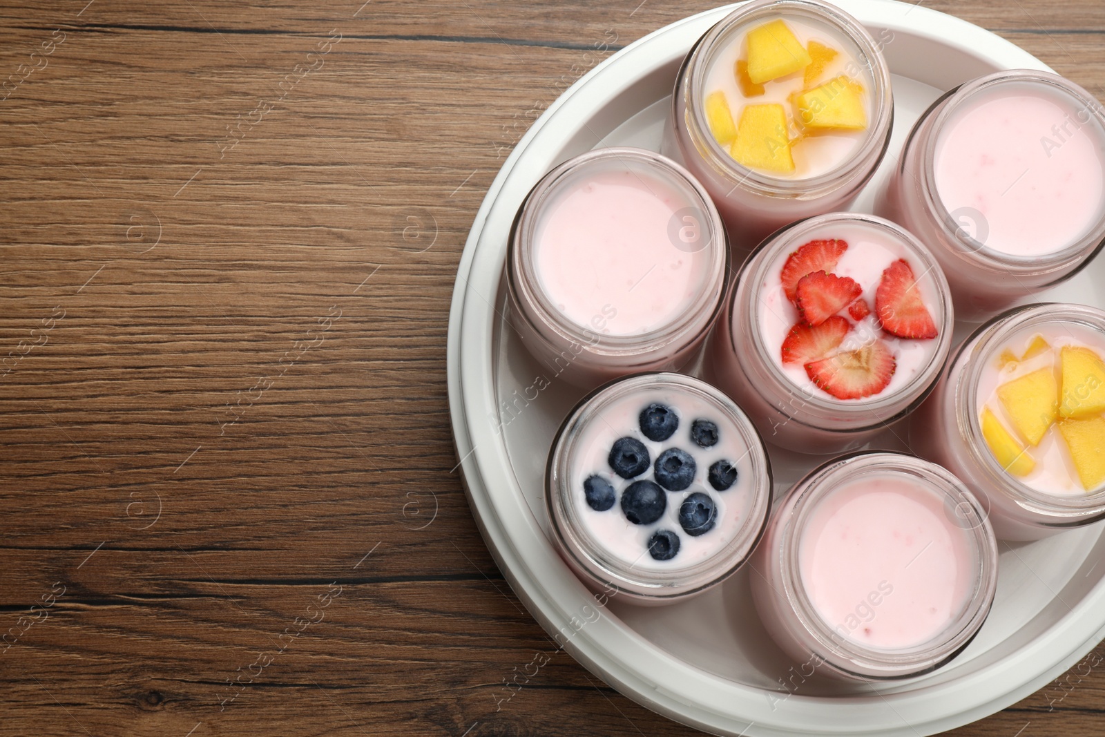 Photo of Yogurt maker with jars and different fruits on wooden table, top view. Space for text